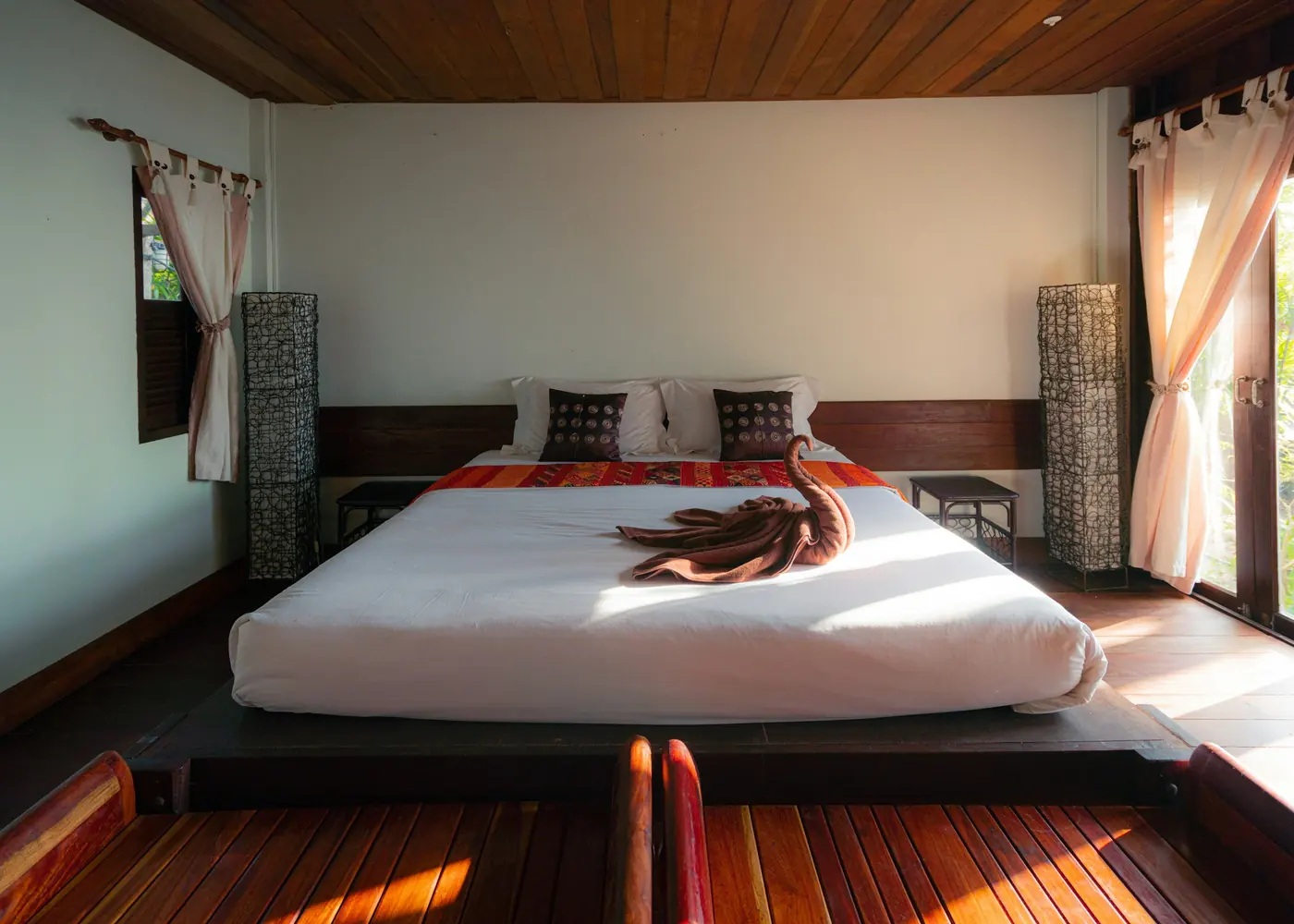 A low bed in a room with timber ceiling and sheer curtains
