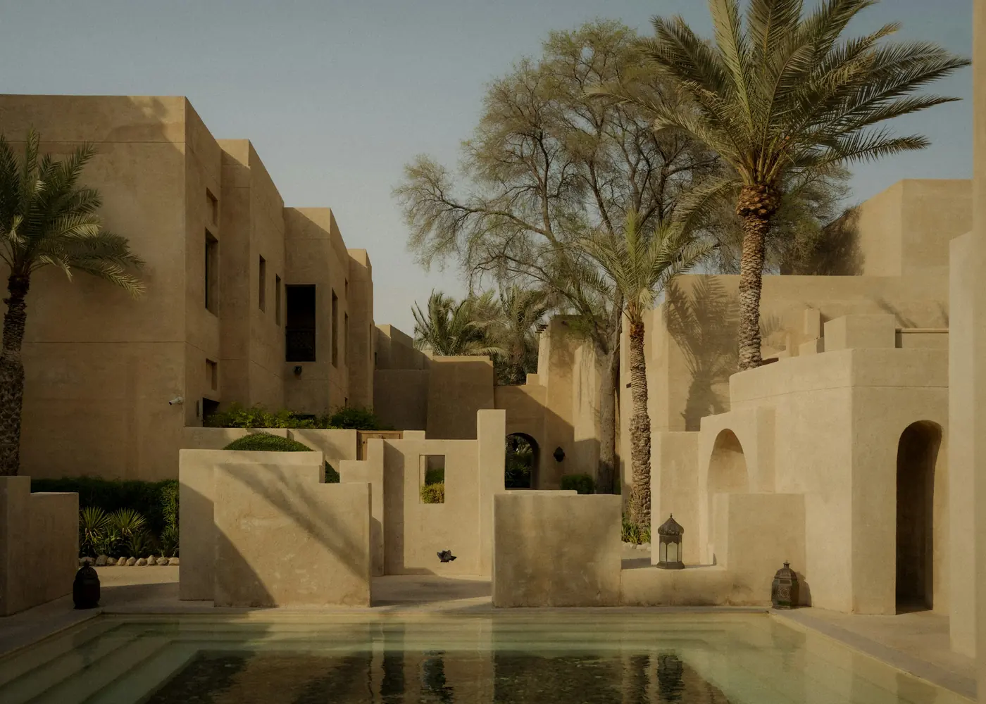 Sandstone walls and palms around a still pool